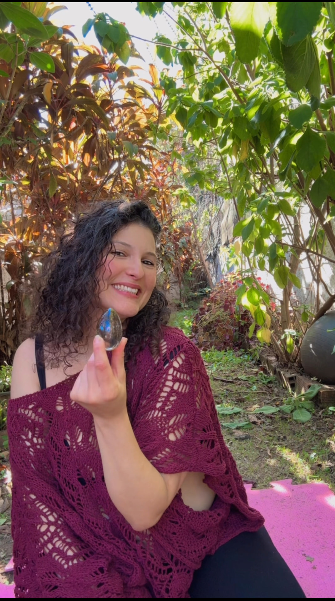 Auriel dos Anjos sentada no jardim, sorrindo, com um Yoni Egg na mão